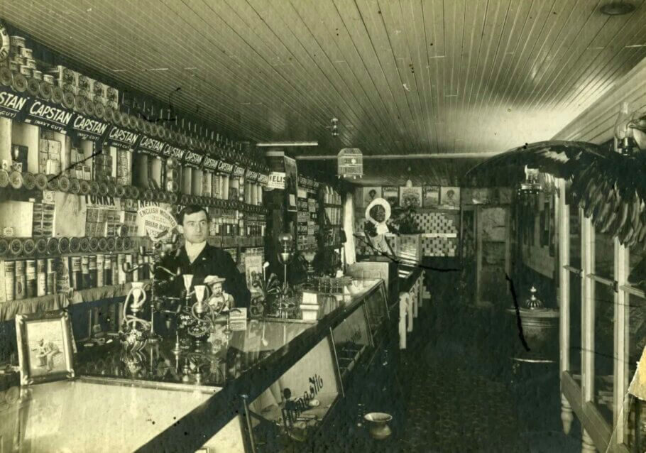Vintage Headshop. Roy Smythe in his 'pool hall and tobacco shop' selling hookahs and pipes, with opium pipes under the glass counter. Revelstoke, British Columbia, 1903